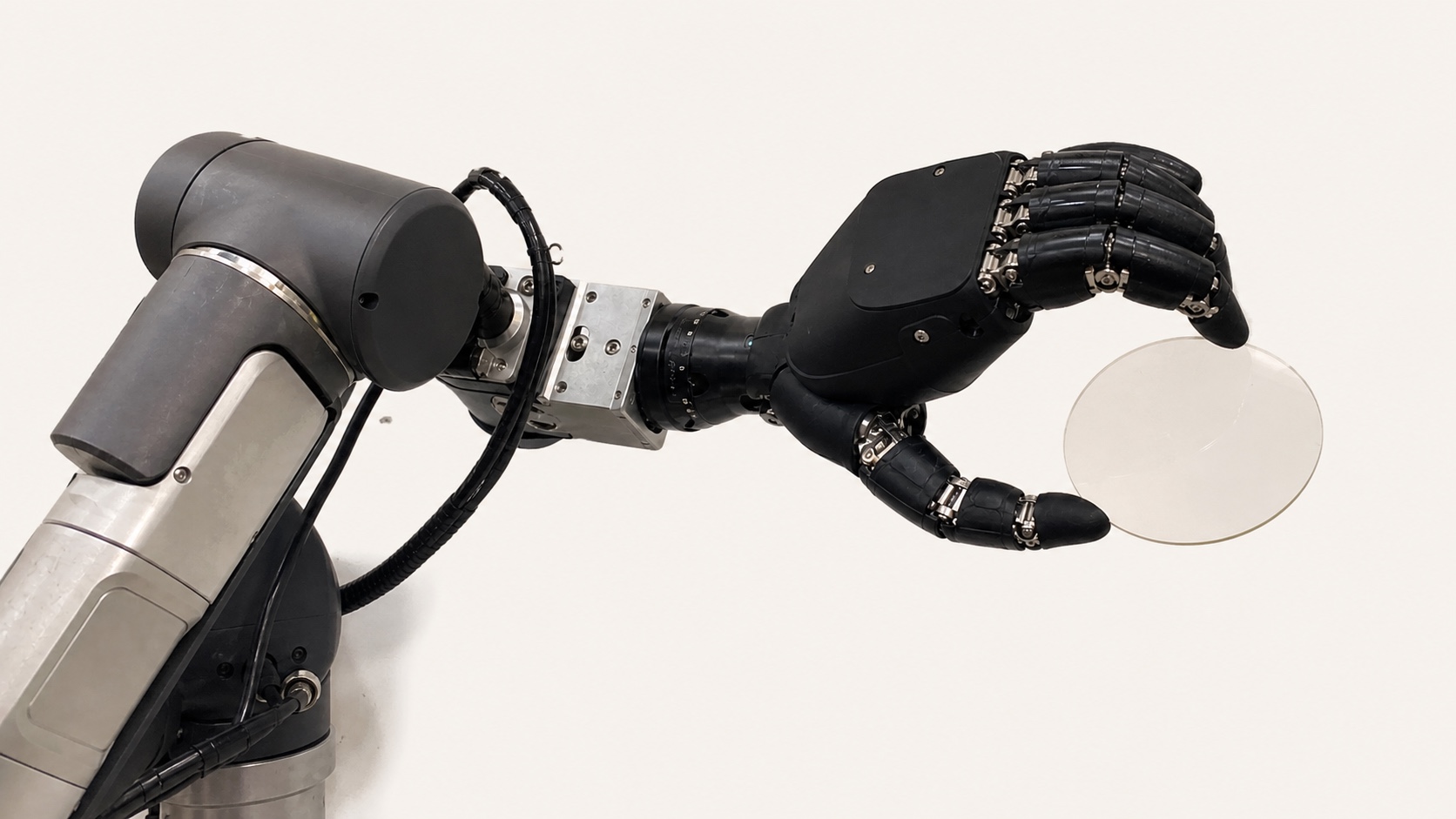 ロボットアーム先端の多指ハンドが、透明なガラスレンズ状の割れやすい部品を保持している。
